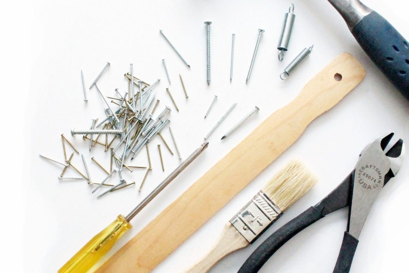 Kleinstreparaturen Werkzeuge: Schraubendreher, Pinsel, Zange und Nägel auf einem hellen Untergrund.