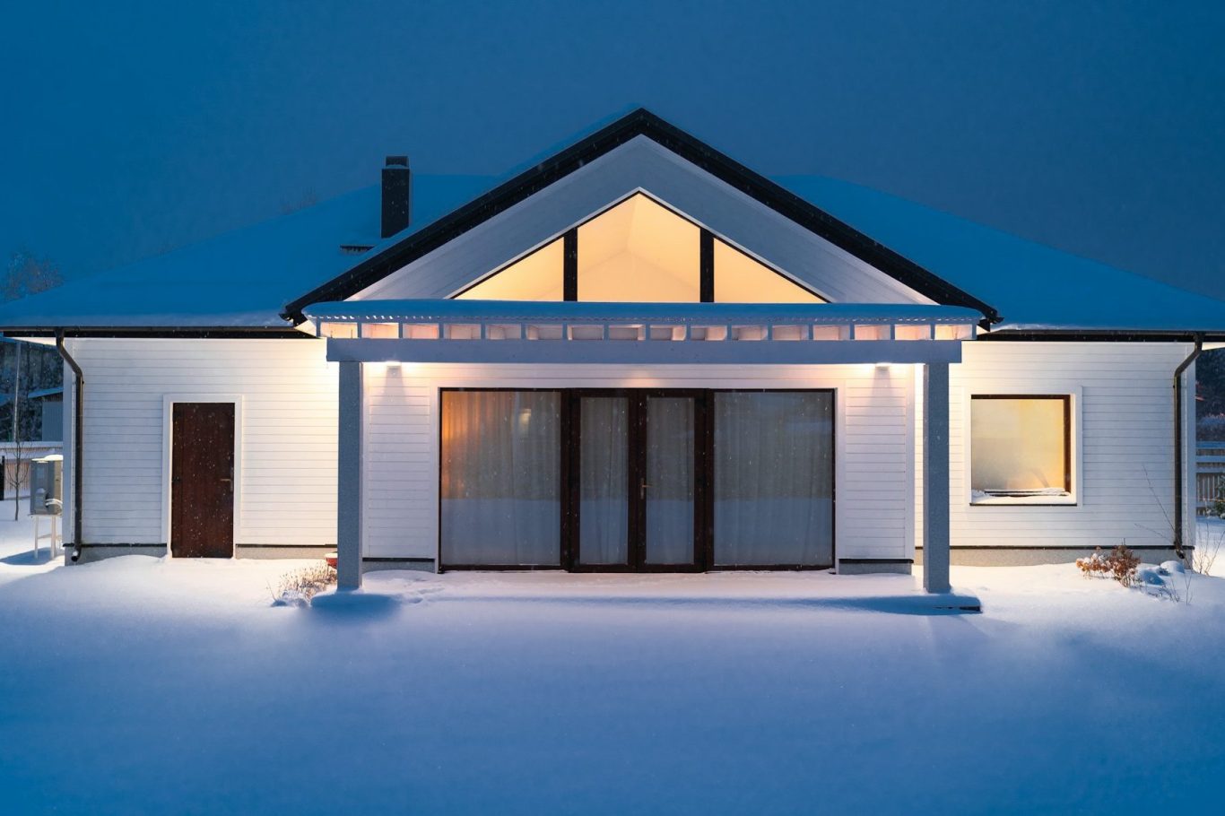 Urlaubsservice Ein modernes Haus im Schnee, beleuchtet bei Dämmerung.
